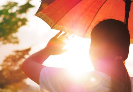 Girl holding an umbrella and raising her hand to block hot sunlight.